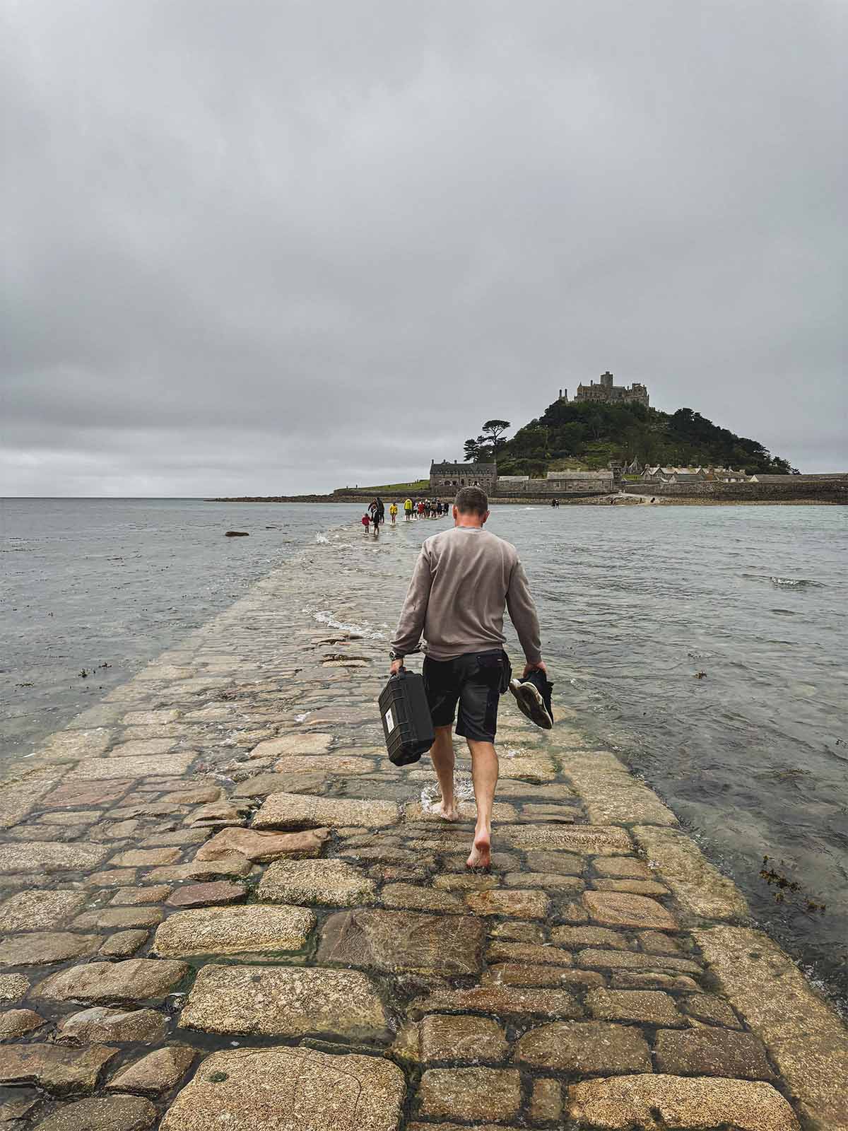 turista che cammina sulla passerella di pietra mentre si sta alzando la marea in Cornovaglia.